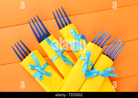 Il blu delle forcelle di plastica avvolto in carta gialla di tovaglioli, il colore di sfondo di legno Foto Stock