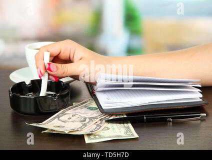 Mano con la sigaretta, notebook, su sfondo lucido Foto Stock