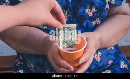 Vecchia donna mendica l elemosina. Vista dettagliata del denaro e monete in mano della povera donna. I problemi sociali della società Foto Stock