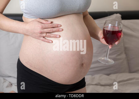Donna incinta bere alcool, ragazza in gravidanza tenendo un bicchiere di vino. Malsano stile di vita. Patologia questione sociale Foto Stock