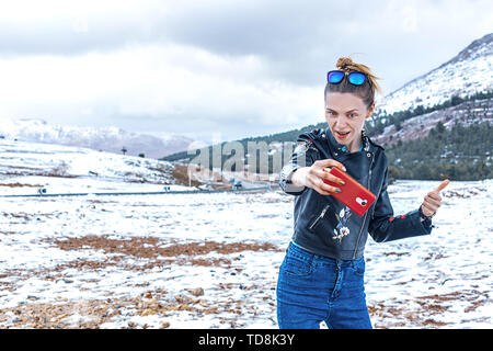 Una giovane e bella donna slava con un sorriso rende un selfie in natura contro lo sfondo delle montagne innevate in inverno. Il Marocco Foto Stock