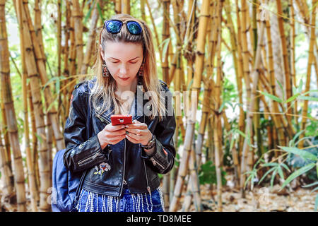 Una ragazza con i capelli biondi è alla ricerca di qualcosa nel telefono mentre è in piedi direttamente alla telecamera con la sua testa piegata. Il Marocco Foto Stock