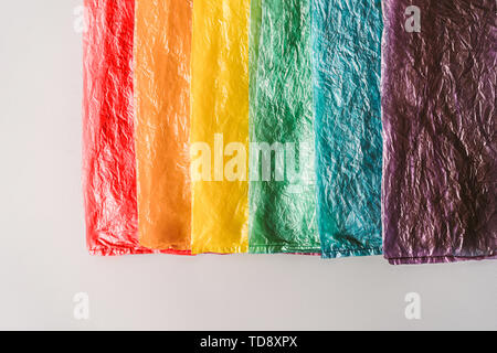 Sacchetti di plastica in una fila con i colori del arcobaleno su sfondo grigio. Foto Stock