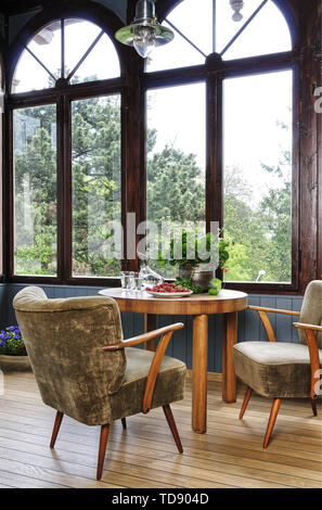 Due sedie imbottite ad una tavola rotonda di fronte a finestre ad arco con vista che dà sul giardino del Regno Unito e irlandese solo diritti Foto Stock