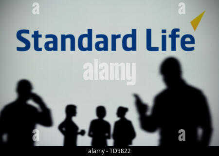 La Standard Life logo è visibile su uno schermo a LED in background mentre si profila una persona utilizza uno smartphone in primo piano (solo uso editoriale) Foto Stock