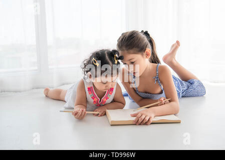 Felice due sorella disegno nel disegno libro insieme a casa. Lo stile di vita delle persone e bambini a giocare. L'istruzione e i bambini del concetto. Diverse etnie e età Foto Stock