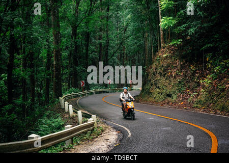 Uomo con zaino siede sulla strada attraverso Bilar verde foresta Man-Made, Bohol, Filippine Foto Stock