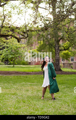 Laureato sul suo college campus in un cappuccio e camice celebrando la laurea da lei undergrad laurea durante la primavera. Foto Stock