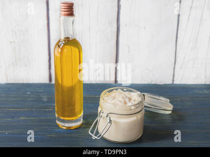 In casa la crema per il viso di olio di argan, in un vasetto di vetro con una bottiglia di olio al lato su un sfondo di legno Foto Stock