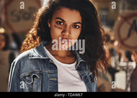 Close up di afro american donna con potenza di parola guardando la telecamera durante una protesta con un gruppo di attivisti femmina all'aperto sulla strada. Diritti dell'uomo. Demo Foto Stock