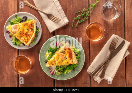 Fette di torta francese con salmone, con insalata verde foglie di alloro, timo e vino bianco, girato dalla parte superiore al buio su un rustico sfondo di legno Foto Stock