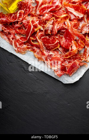 Stuzzicanti fette di prosciutto iberico in primo piano. Olio d'oliva. Sfondo nero. Spazio per inserire il tuo testo. Foto Stock