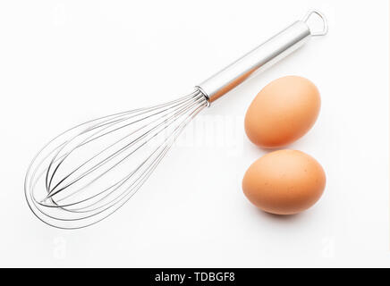 Cucina metallica aste manualmente per la miscelazione di prodotti alimentari con 2 uova fresche (collezione di oggetti da cucina). Isolato su sfondo bianco. Foto Stock