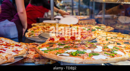 Pizzeria La finestra di vetro. Varietà di pizze italiane in un negozio di display, cibo di strada. Cucina lavoratori disponendo le pizze. Foto Stock