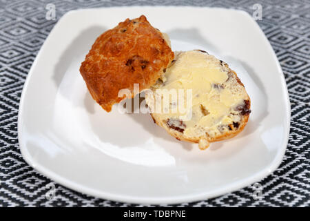 Frutto scone con confettura di fragole e panna montata su una piastra bianca con una tazza di tè in una tazza modellato Foto Stock