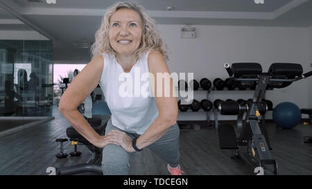 Donna anziana rende squattings in palestra. Donna anziana donna Senior fa un sport esercizi in palestra. Foto Stock