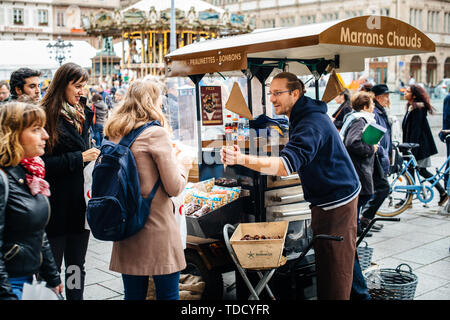 Strasburgo, Francia - 28 OTT 2017: ambulatoriamente venditore maschio a caldo di castagne marron chauds sulle strade della città francese di servire i clienti con cibo organico tradizionale alsaziana cibo di strada Foto Stock