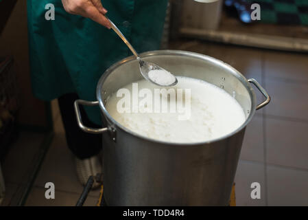 La cottura di ricotta e formaggio in casa. L'uomo crea il formaggio, il riscaldamento di latte e siero di latte in un recipiente di alluminio. In casa rustico prodotti lattiero-caseari Foto Stock