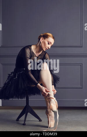 Ballerina in un nero tutu si siede su una sedia su uno sfondo nero. Foto Stock