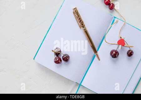 Piatto disposizione laici del notebook vuota ufficiale con la penna accanto ai frutti di bosco freschi su sfondo bianco, vista dall'alto.Il notebook e cuori rossi isolato ,copia Foto Stock