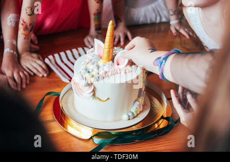 I bambini con le mani in mano bambine raggiungere per la torta. Grande bella torta unicorn sul compleanno di piccola principessa sulla tavola festiva Foto Stock