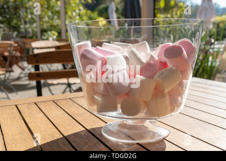 Una vista ravvicinata di colore rosa e bianco marshmallows in una rotonda grande contenitore di vetro su di un tavolo di legno Foto Stock