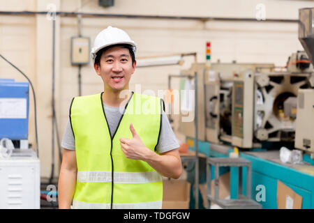 Asian operaio di fabbrica con elmetto di sicurezza poste guardando la fotocamera con sorriso in impianti industriali in industria pesante manufacturing factory. Foto Stock