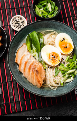 Giapponese ramen zuppa di noodle al pollo con il rosso il tappetino di bambù. Vista dall'alto, con orientamento verticale Foto Stock