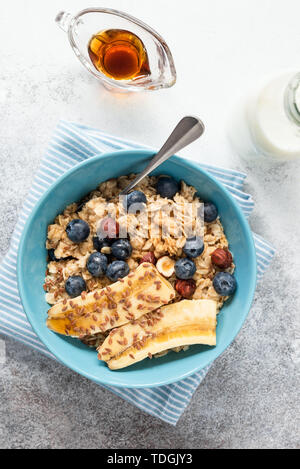 Sana colazione avena porridge ciotola con banana, mirtillo, nocciole e sciroppo d'acero. Tabella vista dall'alto. Pulire mangiare, dieta concetto Foto Stock