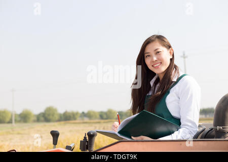 Giovane donna cinese agonomist in golden campo di cereali con piccole harvester Foto Stock