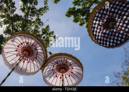 Gruppo di coloratissimi ombrelli Balinese alla cerimonia di celebrazione nel tempio indù. Design tradizionale, bianco e motivo a scacchi sotto l'albero Foto Stock