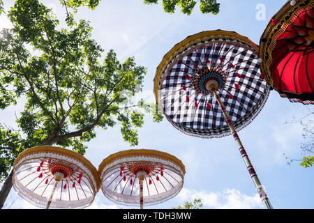 Gruppo di coloratissimi ombrelli Balinese alla cerimonia di celebrazione nel tempio indù. Design tradizionale, bianco e motivo a scacchi sotto l'albero Foto Stock