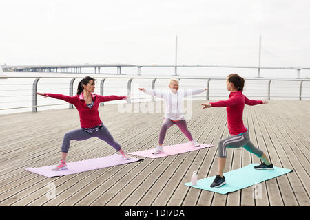 A piena lunghezza ritratto di donna contemporanea facendo yoga all'aperto all'alba dal fiume, spazio di copia Foto Stock