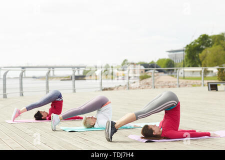 A piena lunghezza ritratto di tre donne contemporanei facendo yoga outdoor e stretching, spazio di copia Foto Stock