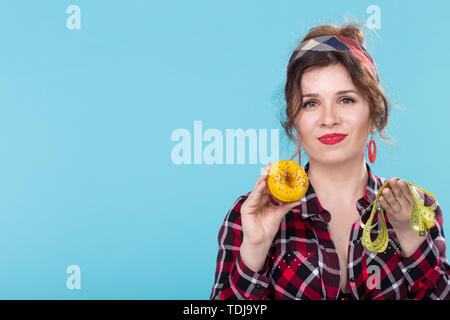 Pin-up donna con nastro di misurazione e la ciambella, copia spazio sopra lo sfondo blu Foto Stock