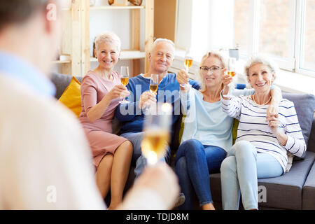 Gruppo di felice spensierato coppia amici seduti su confortevoli divani e abbracciando mentre solleva lo champagne flauti in house party Foto Stock