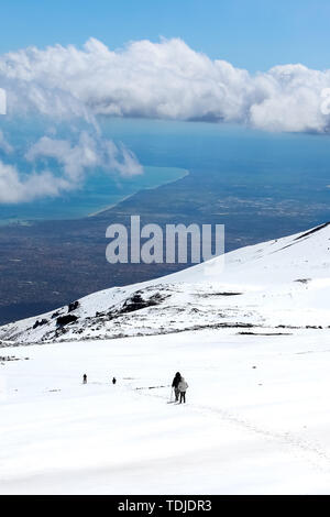 Incredibile paesaggio dal Monte Etna, Sicilia, Italia. Gli escursionisti sulla strada giù dal vulcano. La neve sulla montagna. Mare siciliano costa in background. Meta turistica apprezzata. Foto Stock