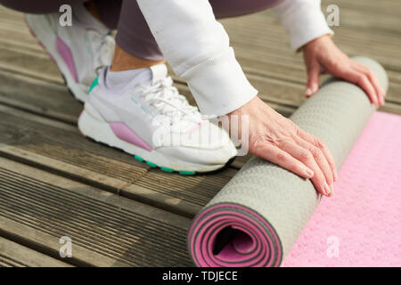 Close up della donna contemporanea bianco da indossare calzature sportive rolling materassino yoga sul molo in legno all'aperto, spazio di copia Foto Stock