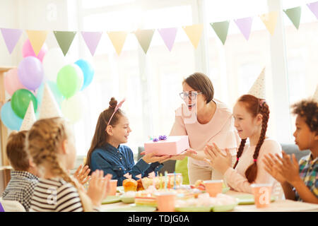 Ritratto di entusiasti bambina ricevere regali durante la festa di compleanno con gli amici, spazio di copia Foto Stock