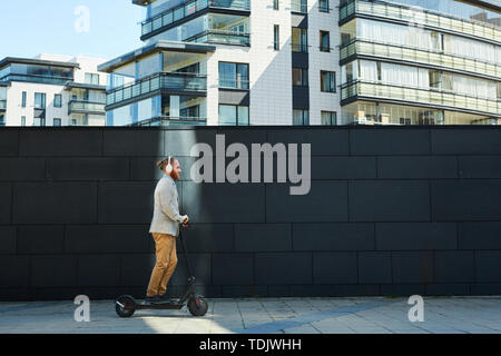 Vista laterale di contenuti sportivo imprenditore tanga in cuffie Calcio Equitazione scooter su strada di città Foto Stock