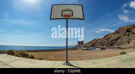 La pallacanestro tavola spinale con cestello sul vecchio campo sportivo. Un enorme edificio abbandonato di fronte all'oceano nel lontano sullo sfondo. Tenerife. Grandangolo, f Foto Stock