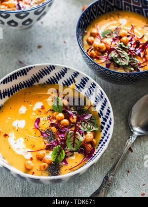 Carota cremosa pastinaca zuppa di acetosella, ceci e microgreens servite in tazze blu su sfondo grigio Foto Stock