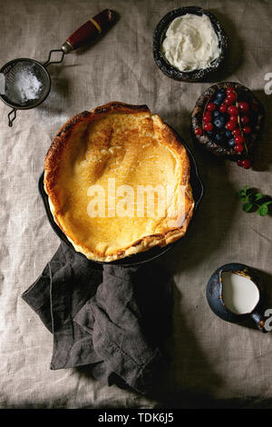 Freschi di forno olandese frittella di bambino in ghisa pan servita con blackberry e rosse bacche Ribes, il mascarpone, lo zucchero in polvere, brocca di crema su gre Foto Stock