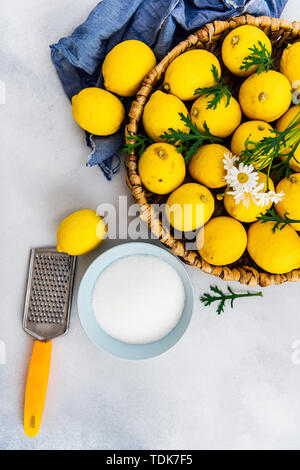 Un cesto pieno di limoni, zucchero granulato in una ciotola blu e una grattugia fotografato su sfondo grigio Foto Stock