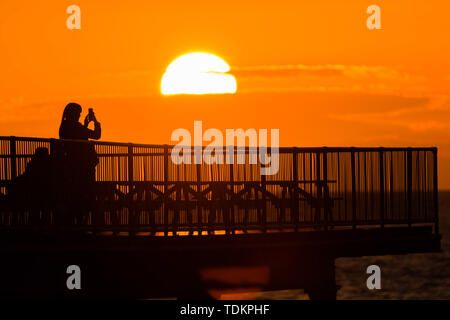 Aberystwyth Wales UK, lunedì 17 giugno 2019 UK Meteo:dopo giorni di pioggia pesante e grigio cielo nuvoloso, un tramonto sulle persone in piedi sul molo a Aberystwyth è un promemoria di ciò che "flaming" Giugno meteo dovrebbe essere ;come Photo credit: keith morris/Alamy Live News Foto Stock