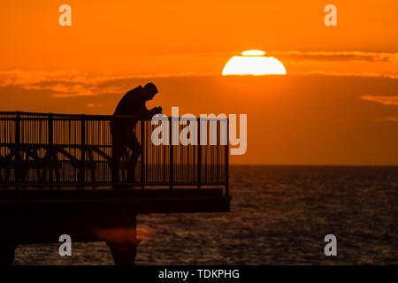 Aberystwyth Wales UK, lunedì 17 giugno 2019 UK Meteo:dopo giorni di pioggia pesante e grigio cielo nuvoloso, un tramonto sulle persone in piedi sul molo a Aberystwyth è un promemoria di ciò che "flaming" Giugno meteo dovrebbe essere ;come Photo credit: keith morris/Alamy Live News Foto Stock