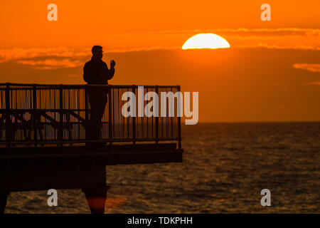 Aberystwyth Wales UK, lunedì 17 giugno 2019 UK Meteo:dopo giorni di pioggia pesante e grigio cielo nuvoloso, un tramonto sulle persone in piedi sul molo a Aberystwyth è un promemoria di ciò che "flaming" Giugno meteo dovrebbe essere ;come Photo credit: keith morris/Alamy Live News Foto Stock