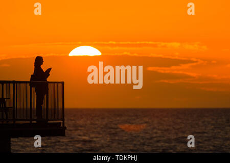 Aberystwyth Wales UK, lunedì 17 giugno 2019 UK Meteo:dopo giorni di pioggia pesante e grigio cielo nuvoloso, un tramonto sulle persone in piedi sul molo a Aberystwyth è un promemoria di ciò che "flaming" Giugno meteo dovrebbe essere ;come Photo credit: keith morris/Alamy Live News Foto Stock