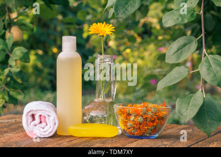 Prodotti per il benessere e gli accessori. Asciugamani, sapone e la bottiglia di plastica con estratto di calendula e di calendula fiori in un pallone di vetro su tavole di legno. Foto Stock