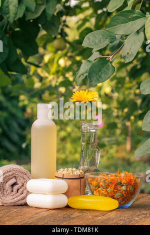 Prodotti per il benessere e gli accessori. Asciugamani, sapone e la bottiglia di plastica con estratto di calendula, calendula fiori in un pallone di vetro e la ciotola di legno con Fiore secco Foto Stock